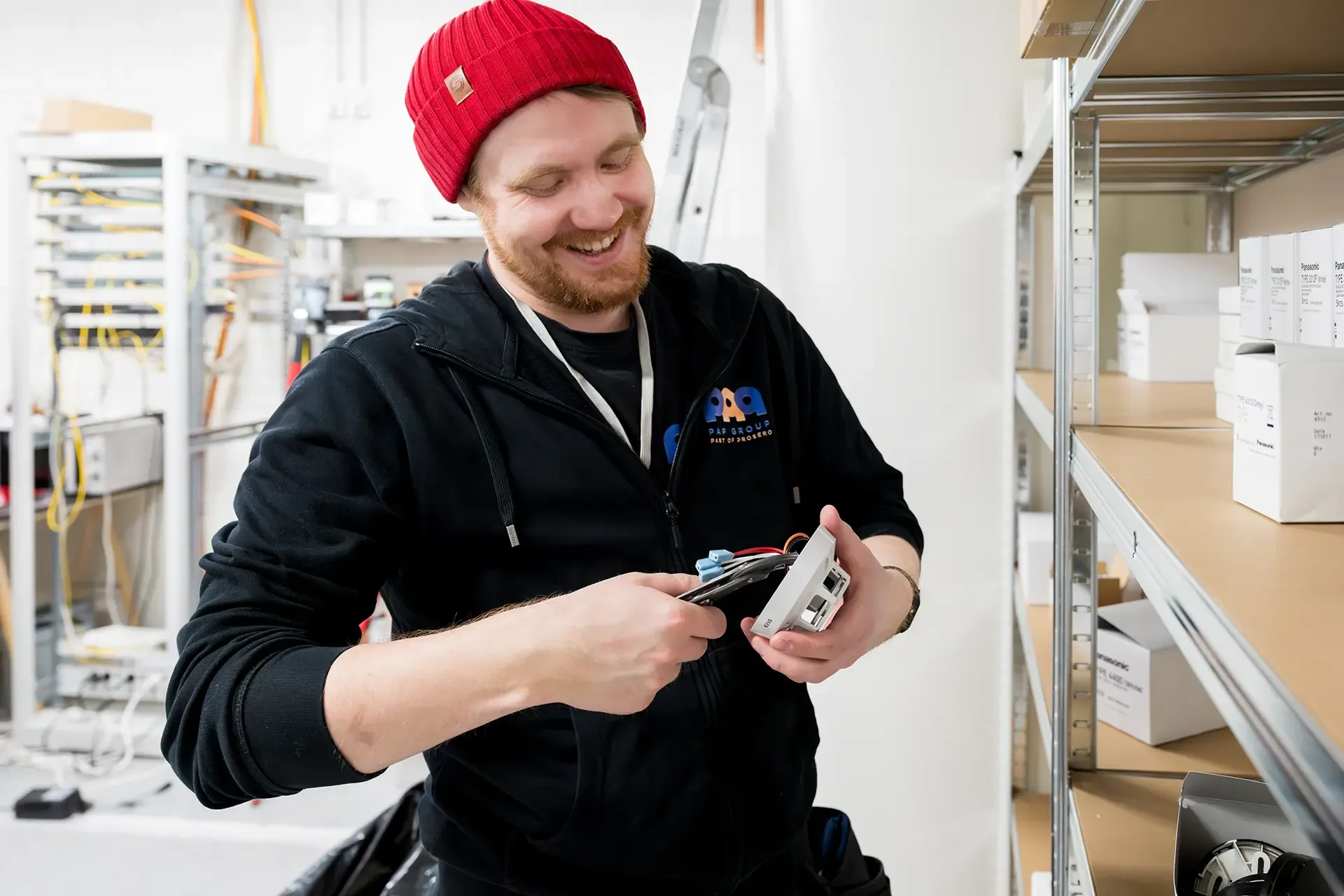A smiling PAP installer connecting wires to a device next to warehouse shelving