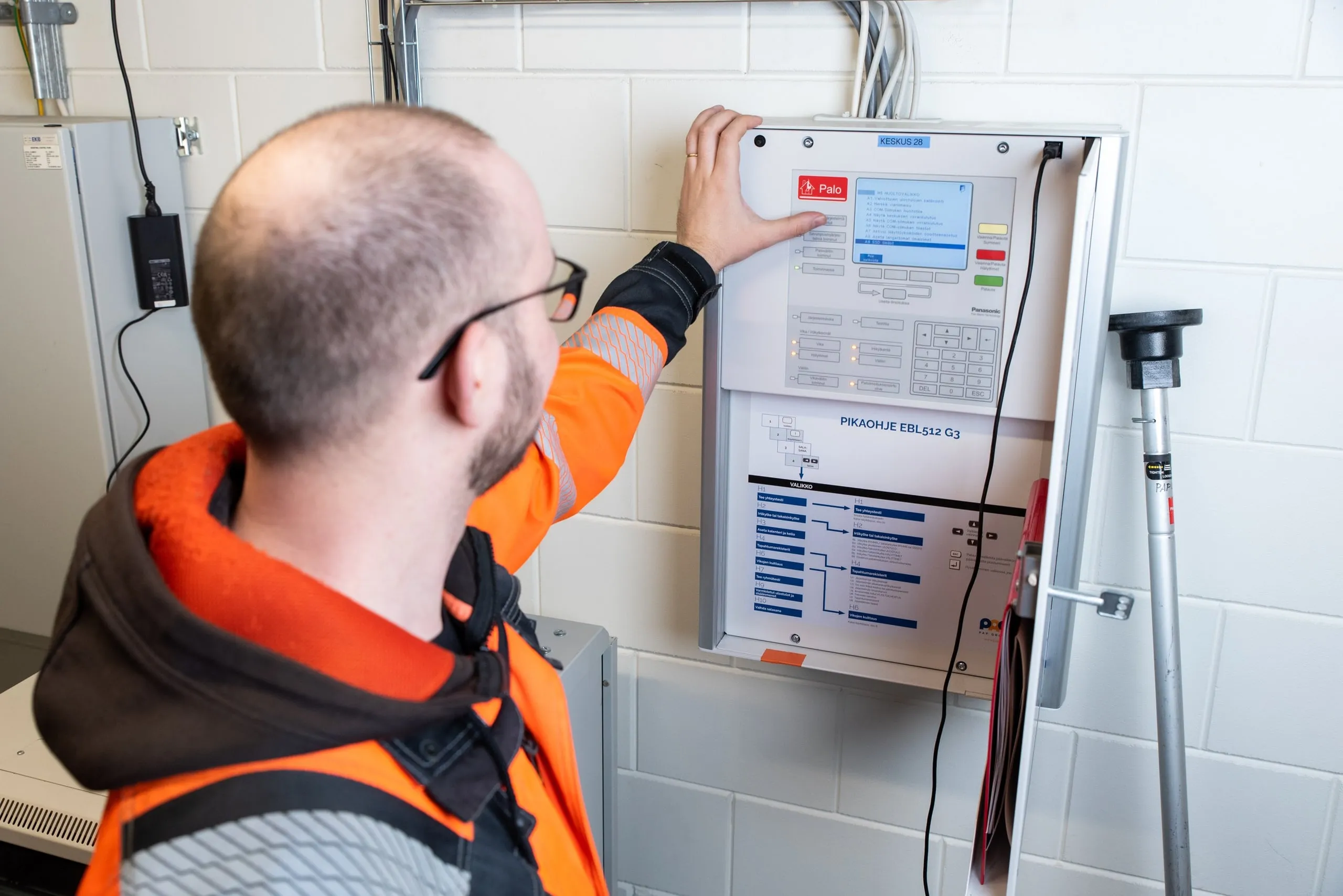 A maintenance technician operating a wall-mounted fire alarm control panel