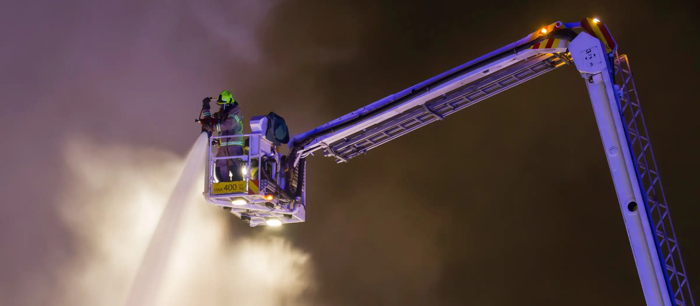 A firefighter in the basket of an aerial platform vehicle fighting a fire with a water jet