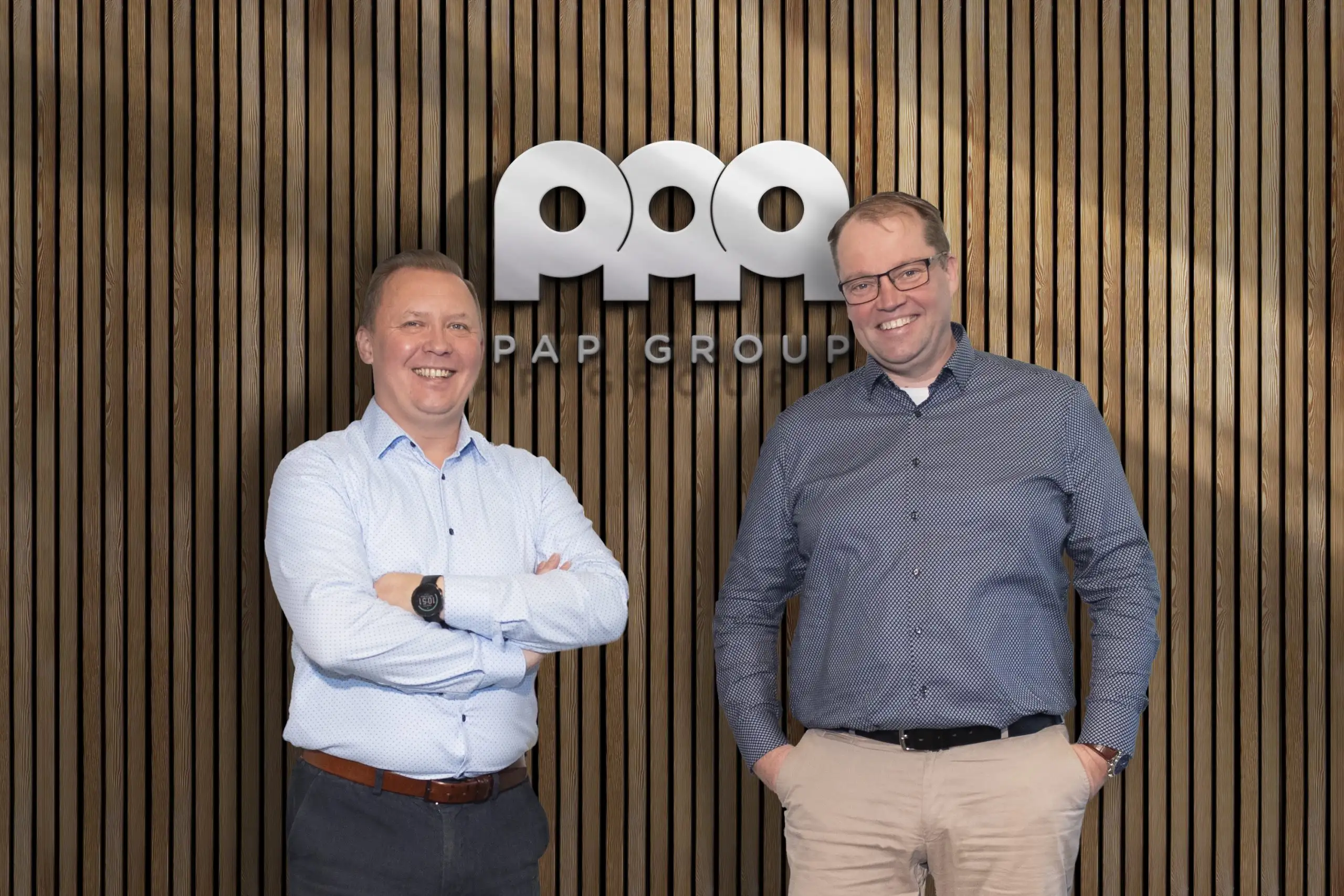 Two men in front of the PAP Group logo next to a wood-panelled wall