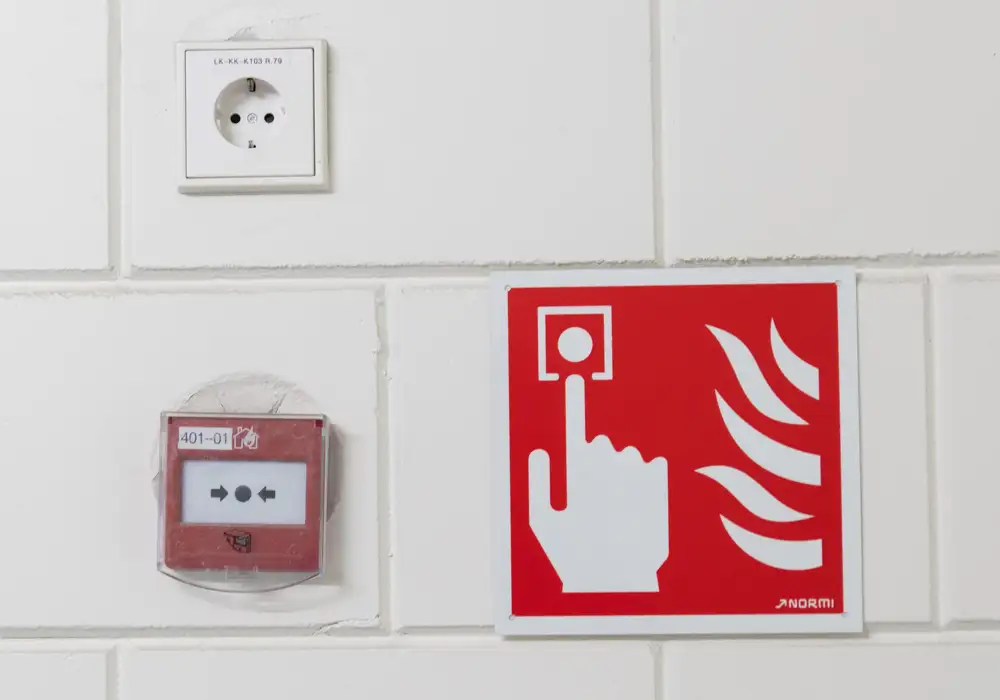 Palopainike ja palopainikkeen opaskyltti valkoisella tiiliseinällä
