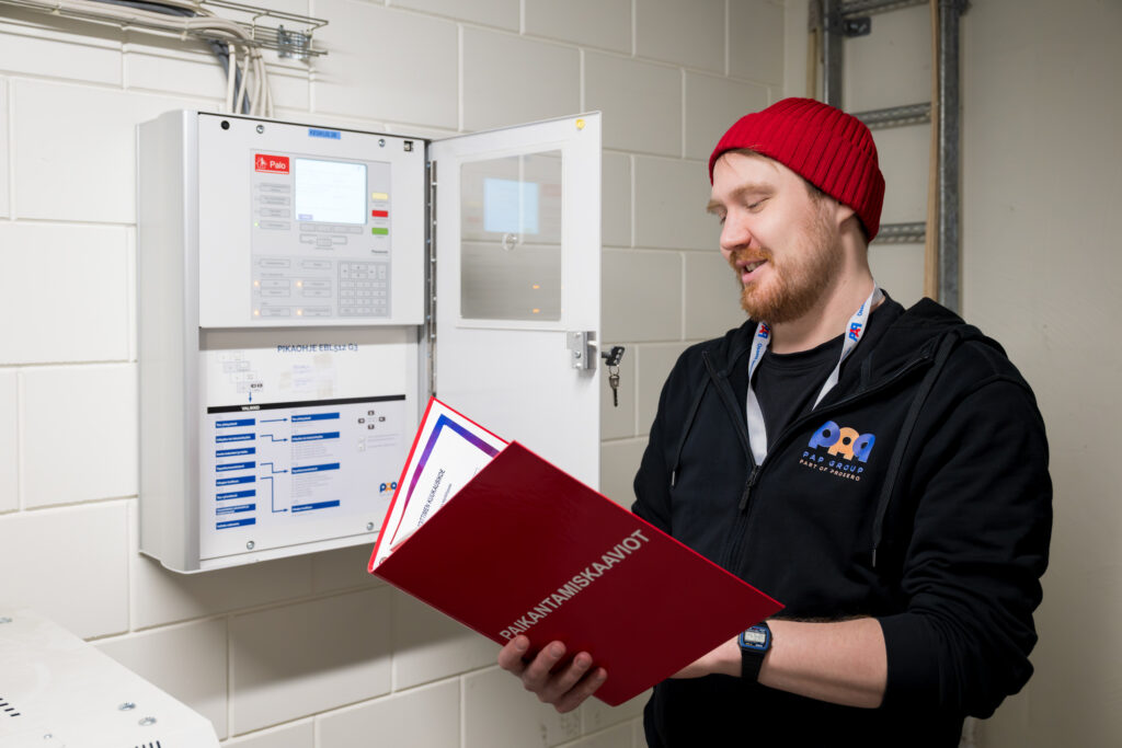 Mies lukee paloilmoitinlaitteen paikantamiskaaviokansiota.